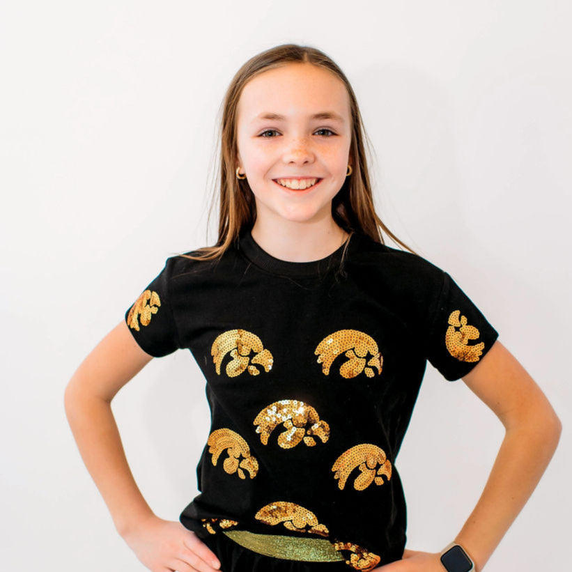 A youth wearing a black short-sleeved t-shirt with gold sequin Tigerhawk logos.
