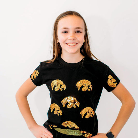 A youth wearing a black short-sleeved t-shirt with gold sequin Tigerhawk logos.